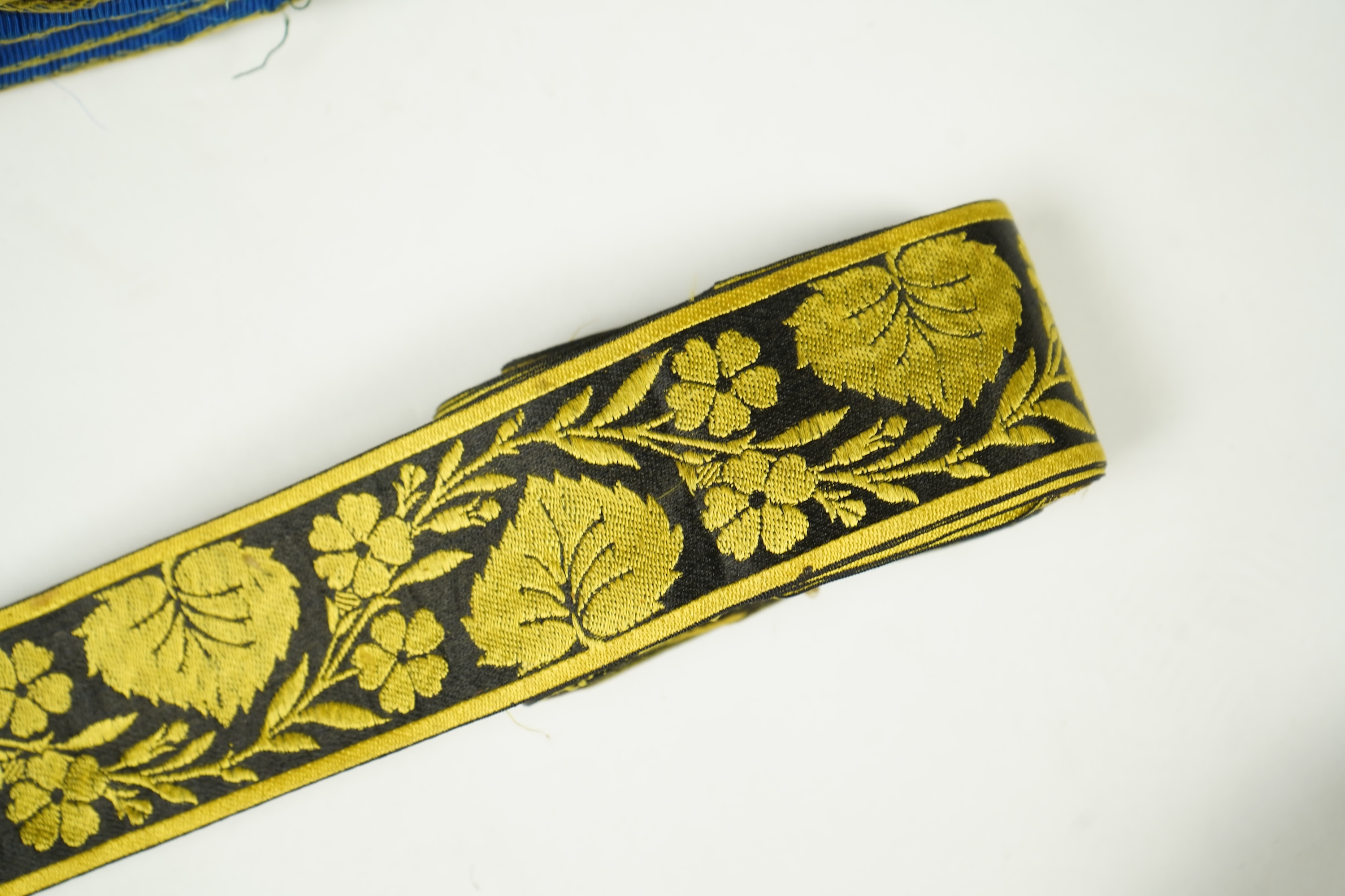 Three long lengths of late 19th century silk woven braiding. One woven in gold, turquoise and maroon silk, possibly for ecclesiastic use, in Christopher Dresser ‘style’ motifs, another in gold and black silk thread in a